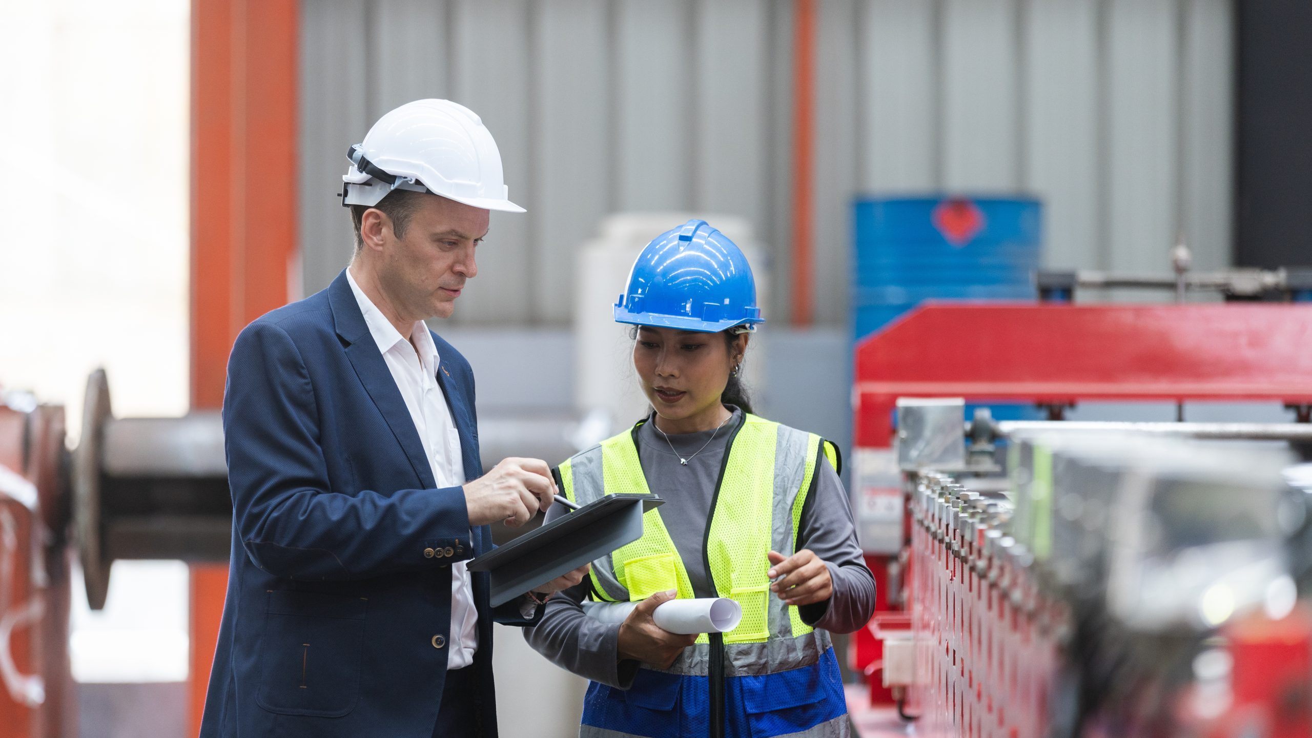 Manager and female worker engineer holding tablet during serious discussion about manufacturing inspection inside large industrial factory with heavy equipment